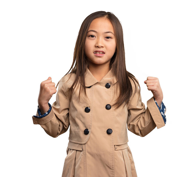 κινεζική κοριτσάκι σε μπεζ trenchcoat κάνει ισχυρή χειρονομία που απομονώνονται σε λευκό φόντο - Φωτογραφία, εικόνα