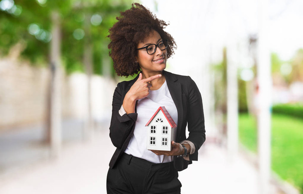 black business woman holding a small house on blurred background - Photo, Image