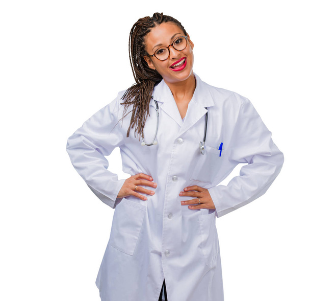 Портрет молодой черной женщины-врача с руками на бедрах, стоящей, расслабленной и улыбающейся, очень позитивной и веселой
 - Фото, изображение
