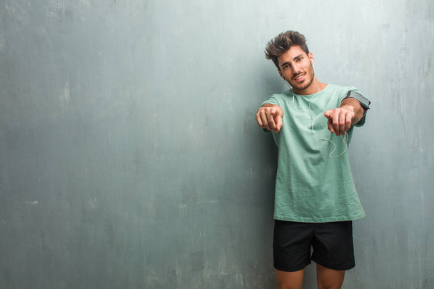 Young fitness man against a grunge wall cheerful and smiling pointing to the front, wearing an armband with phone. - Photo, Image