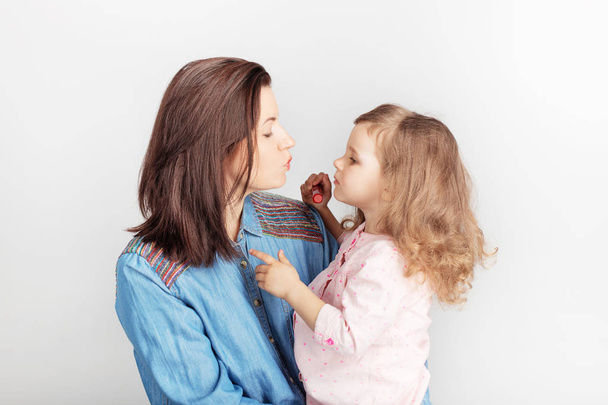 Mother and her child daughter girl with a lipstick. Portrait of a lovely little baby girl and her mum against white background. Funny family! fashion baby girl is doing makeup and having fun.  - Photo, Image