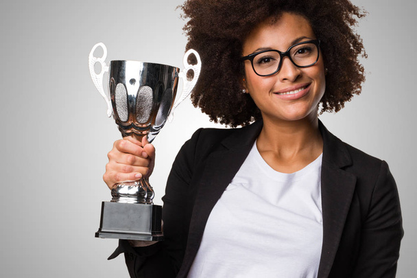 black business woman holding a trophy on gray background - Foto, Imagen
