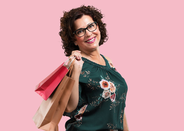 Mujer de mediana edad alegre y sonriente, muy emocionada llevando una bolsa de compras, lista para ir de compras y buscar nuevas ofertas
 - Foto, Imagen