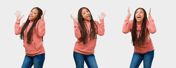 Fitnessgruppe junge schwarze Frau lacht überrascht und hebt die Arme auf grauem Hintergrund - Foto, Bild