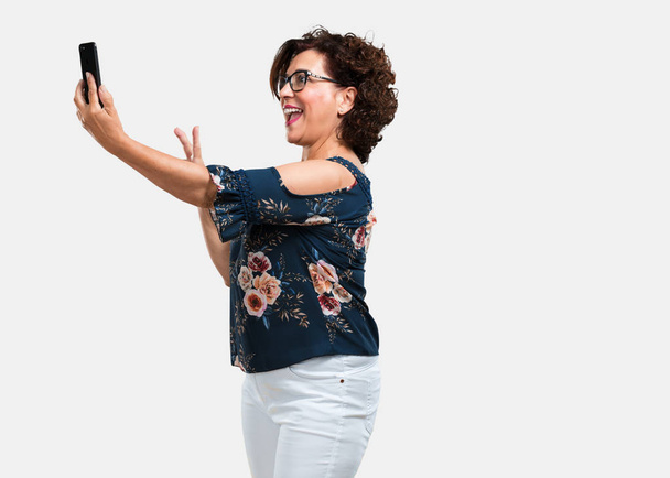 Frau mittleren Alters selbstbewusst und fröhlich, macht ein Selfie, schaut mit einer lustigen und unbeschwerten Geste aufs Handy, surft in den sozialen Netzwerken und im Internet - Foto, Bild