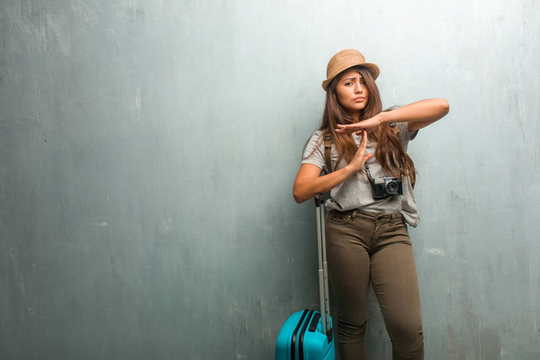 Ritratto di giovane viaggiatore donna latina contro un muro stanco e annoiato, facendo un gesto di timeout, ha bisogno di fermarsi a causa di stress da lavoro, concetto di tempo. Con in mano una valigia blu
. - Foto, immagini