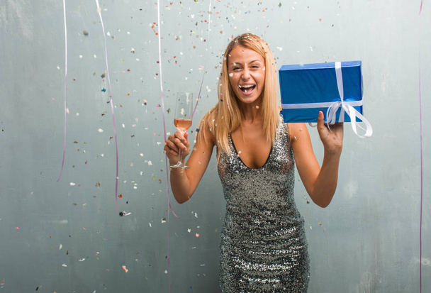 Portrait of elegant young blonde woman drinking champagne and holding a gift, celebrating new year with confetti. - Photo, Image