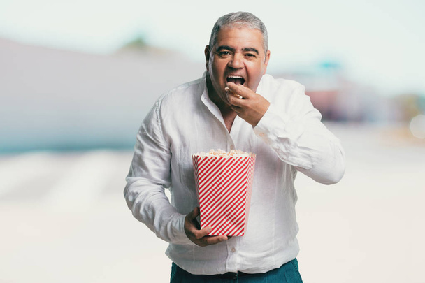 Středního věku člověka šťastná a spokojená, drží prokládané popcorn kbelík, překvapil nový film, oči otevřené a obdiv - Fotografie, Obrázek
