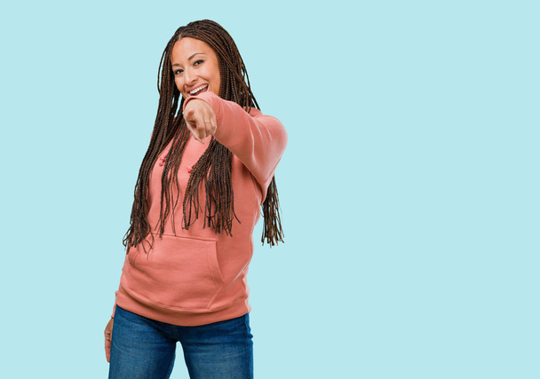 Портрет молодої чорної жінки, що носить коси весело і усміхнено вказує на передній план
 - Фото, зображення