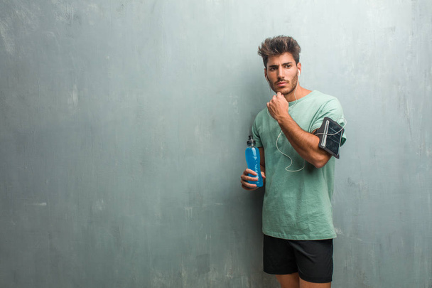 Young fitness man against a grunge wall thinking and holding a blue energy drink. - Photo, Image