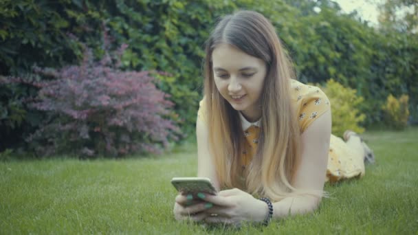 Footage pretty girl using app on her smartphone near tree in the park. - Filmati, video