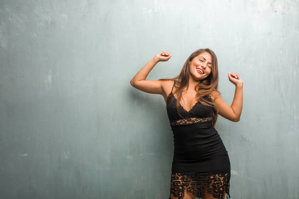 Portrait of young pretty woman wearing a dress against a wall listening to music, dancing and having fun, moving, shouting and expressing happiness, freedom concept - Foto, imagen