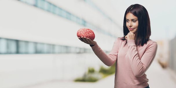 Young pretty woman thinking and deducting, looking at a brain trying to understand it, concept of intelligence and science in the university campus - Foto, Imagen