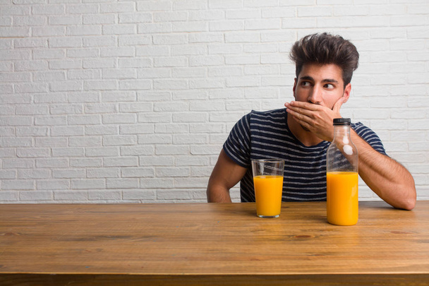 Természetes és jóképű fiatalember ül egy asztal, száj, szimbólum, a csend és az elnyomás, amely nem próbál mondani valamit. A reggeli elfogyasztására, magában foglalja a narancs juice és a gabonafélék tál. - Fotó, kép