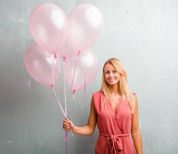 Elegante joven rubia sosteniendo globos rosados contra una pared
. - Foto, imagen