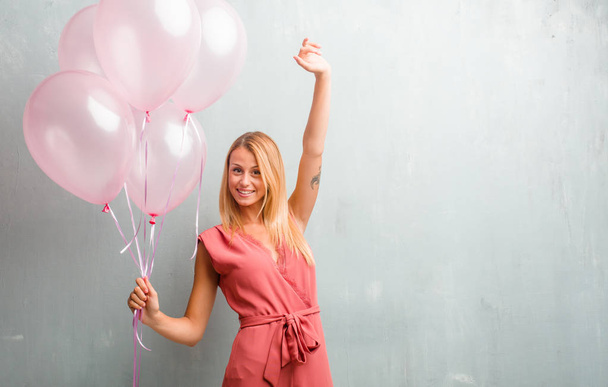 Tyylikäs nuori blondi nainen, jolla on vaaleanpunainen ilmapalloja seinää vasten
. - Valokuva, kuva