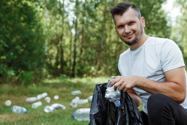Werken als vrijwilliger, vrijwilliger. Een mannelijke vrijwilliger die een vuilniszak verzamelt kunststof. Concept reinigen van aard van plastic, vervuiling. - Foto, afbeelding