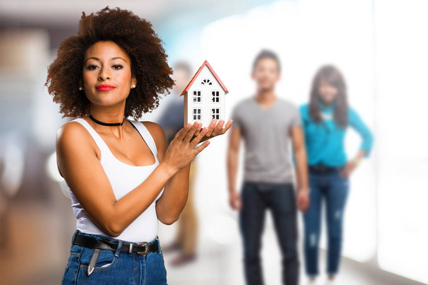 jeune femme noire tenant un petit modèle de maison avec des personnes floues en arrière-plan
 - Photo, image
