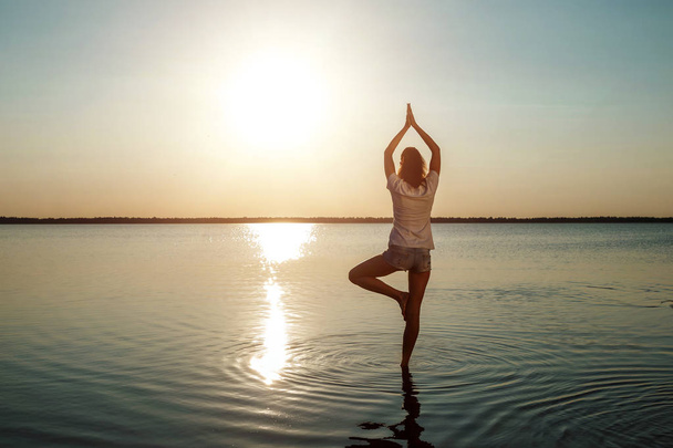 Young girl silhouette, yoga on nature, on a background of a lake and beautiful sunset. Fresh air, healthy way of life, - Photo, Image