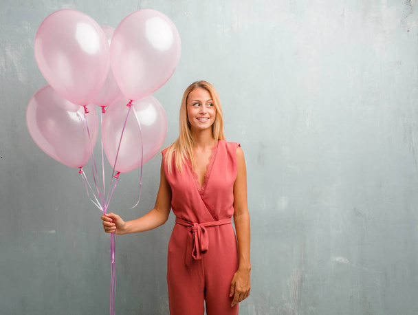 elegante junge blonde Frau hält rosa Luftballons an eine Wand. - Foto, Bild