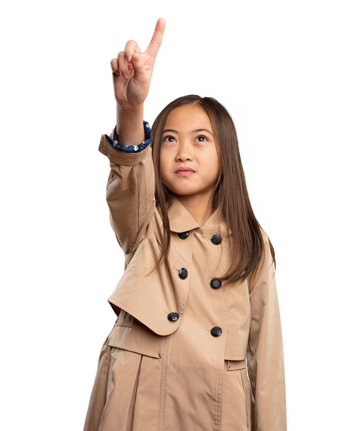 κινεζική κοριτσάκι σε μπεζ trenchcoat αγγίζοντας την οθόνη που απομονώνονται σε λευκό φόντο - Φωτογραφία, εικόνα