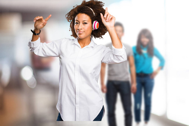 junge schwarze Frau trägt Kopfhörer und tanzt mit verschwommenen Menschen im Hintergrund - Foto, Bild