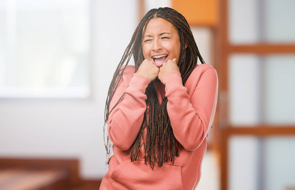 Portrait of a young black woman wearing braids very happy and excited, raising arms, celebrating a victory or success, winning the lottery - Foto, afbeelding
