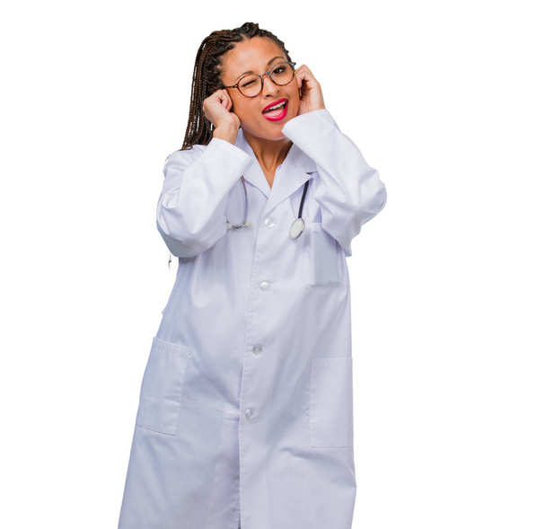Portrait of a young black doctor woman covering ears with hands, angry and tired of hearing some sound - Foto, Imagem