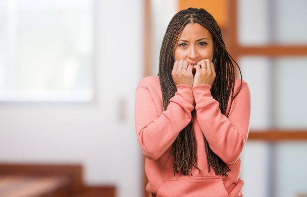 Retrato de uma jovem negra usando tranças mordendo unhas, nervosa e muito ansiosa e assustada com o futuro, sente pânico e estresse
 - Foto, Imagem