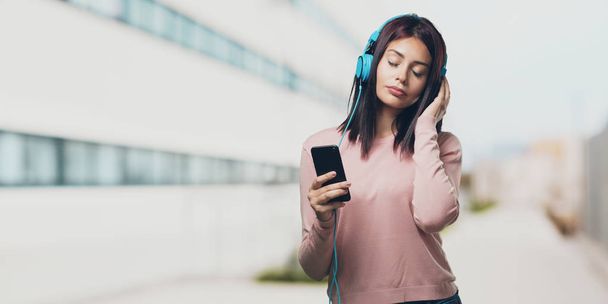 junge hübsche Frau entspannt und konzentriert, hört Musik mit seinem Handy, spürt den Rhythmus und entdeckt neue Künstler, Augen zu und durch auf dem Universitätscampus - Foto, Bild