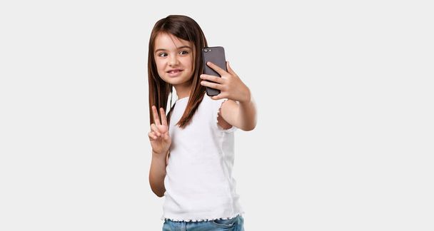 Volledige lichaam meisje zelfverzekerd en vrolijk, een selfie nemen, kijken naar de mobiele telefoon met een grappig en zorgeloze gebaar, de sociale netwerken en het internet surfen - Foto, afbeelding