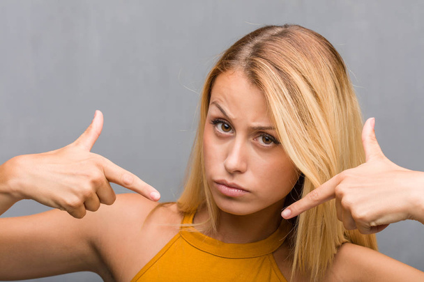 Porträt einer natürlichen jungen blonden Frau, die mit dem Finger zeigt, Beispiel zu folgen - Foto, Bild