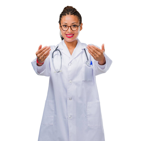 Portrait of a young black doctor woman inviting to come, confident and smiling making a gesture with hand, being positive and friendly - Fotografie, Obrázek