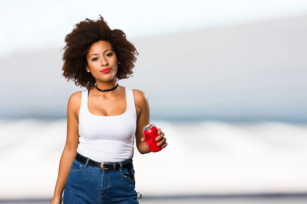 young black woman holding soda can on blurred background - Photo, Image