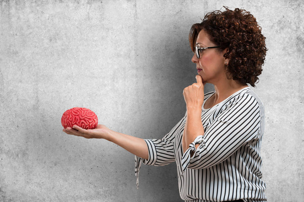 W średnim wieku kobieta myśli i odliczeniu, patrząc na mózg stara się zrozumieć to pojęcie inteligencji i nauka - Zdjęcie, obraz