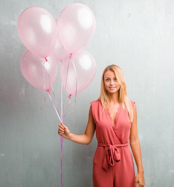 Elegáns fiatal szőke nő gazdaság rózsaszín léggömbök a falhoz. - Fotó, kép