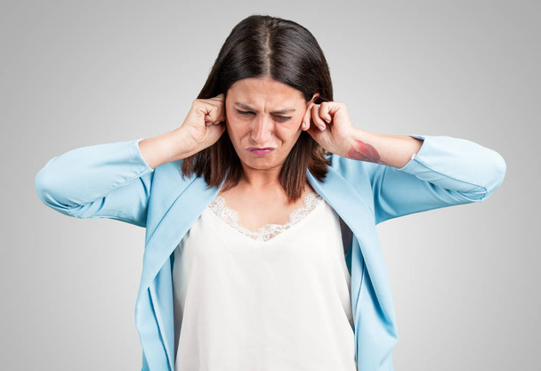 Mujer de mediana edad cubriendo los oídos con las manos, enojada y cansada de escuchar algún sonido
 - Foto, Imagen