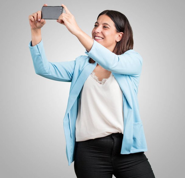 Middle aged woman confident and cheerful, taking a selfie, looking at the mobile with a funny and carefree gesture, surfing the social networks and internet - Photo, image