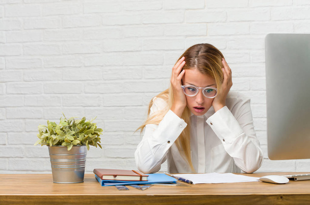 Porträt einer jungen Studentin, die auf ihrem Schreibtisch sitzt und frustriert und verzweifelt Aufgaben erledigt, wütend und traurig mit den Händen auf dem Kopf - Foto, Bild