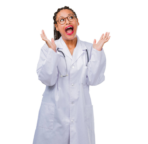 Portrait of a young black doctor woman surprised and shocked, looking with wide eyes, excited by an offer or by a new job, win concept - Photo, image