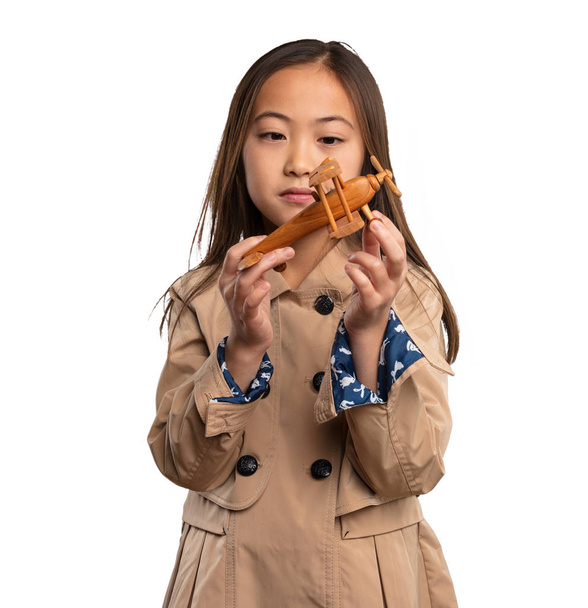Beyaz arka plan üzerinde izole bir uçak holding bej trençkot, Çinli küçük kız - Fotoğraf, Görsel