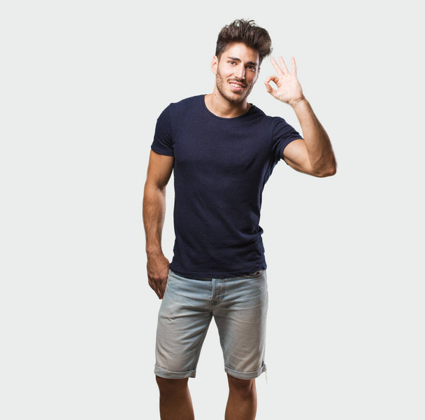 Young handsome man standing cheerful and confident doing ok gesture, excited and screaming, concept of approval and success - Fotoğraf, Görsel