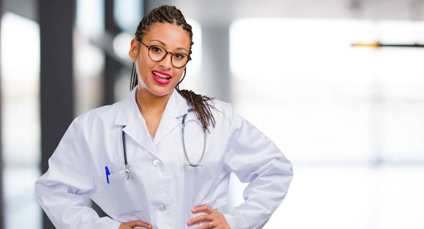 Портрет молодої чорної жінки-лікаря з руками на стегнах, стоячи, розслабляючись і усміхаючись, дуже позитивний і веселий
 - Фото, зображення