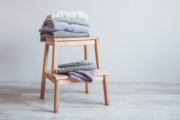 Stack of cozy knitted clothes on a wooden ladder. Gray wall. Vintage tinting - Photo, image