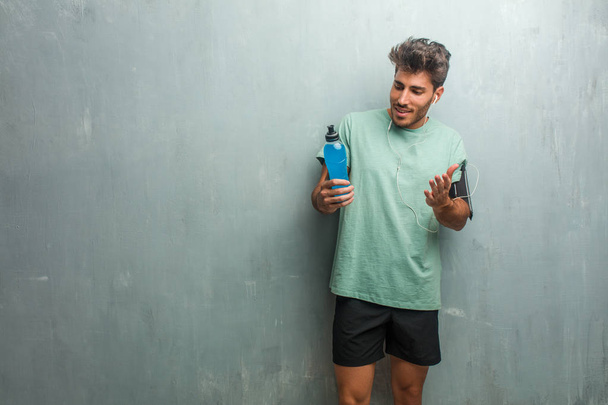 Jeune homme de remise en forme contre un mur grognant surpris et choqué tenant une boisson d'énergie bleue
. - Photo, image