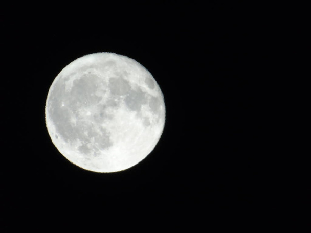 Een geweldige fotografie van het volle maanlicht onder een donkere lucht met enkele kleine sterren op de achtergrond - Foto, afbeelding