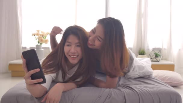 Beautiful young asian women LGBT lesbian happy couple sitting on bed hug and using phone taking selfie together bedroom at home. LGBT lesbian couple together indoors concept. Spending nice time home. - Footage, Video