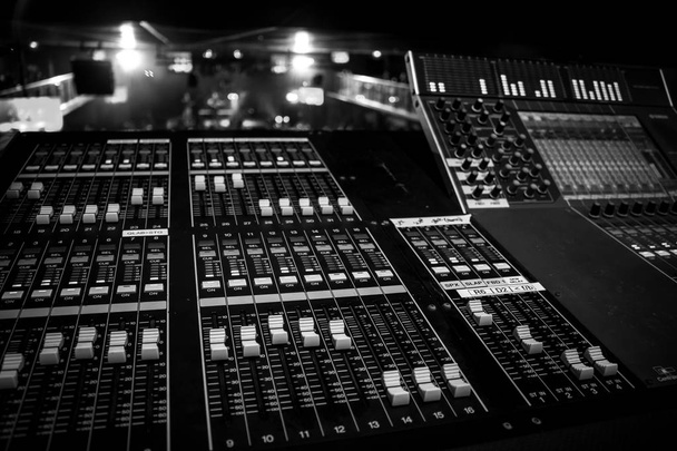 Wide view of Professional Audio Sound Mixing Console with artist performing in distant  background, monochrome black and white style - Photo, Image