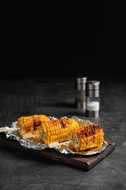 Delicious grilled corn cobs on table against black background. Space for text - Photo, Image