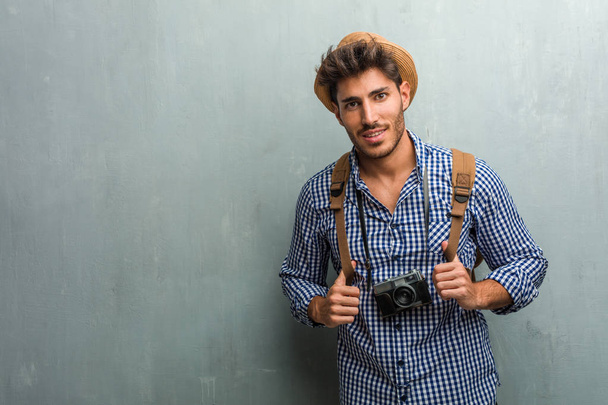 Young handsome traveler man wearing a straw hat, a backpack and a photo camera cheerful and with a big smile, confident, friendly and sincere, expressing positivity and success - Φωτογραφία, εικόνα